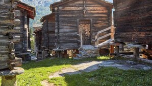 Un edificio rústico de madera con una escalera de piedra, rodeado por un paisaje montañoso.