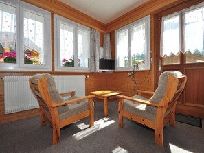 A cozy room with wooden walls, a radiator, two wooden chairs, a small table, and a TV mounted on the wall. - Chalet Ideal Appartement/Fewo 2-Bettwohnung Nr. 1 by Interhome (Saas-Fee)