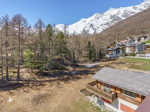 Un bâtiment de style chalet, avec un toit en pierre, entouré d’une forêt et de montagnes aux sommets enneigés.