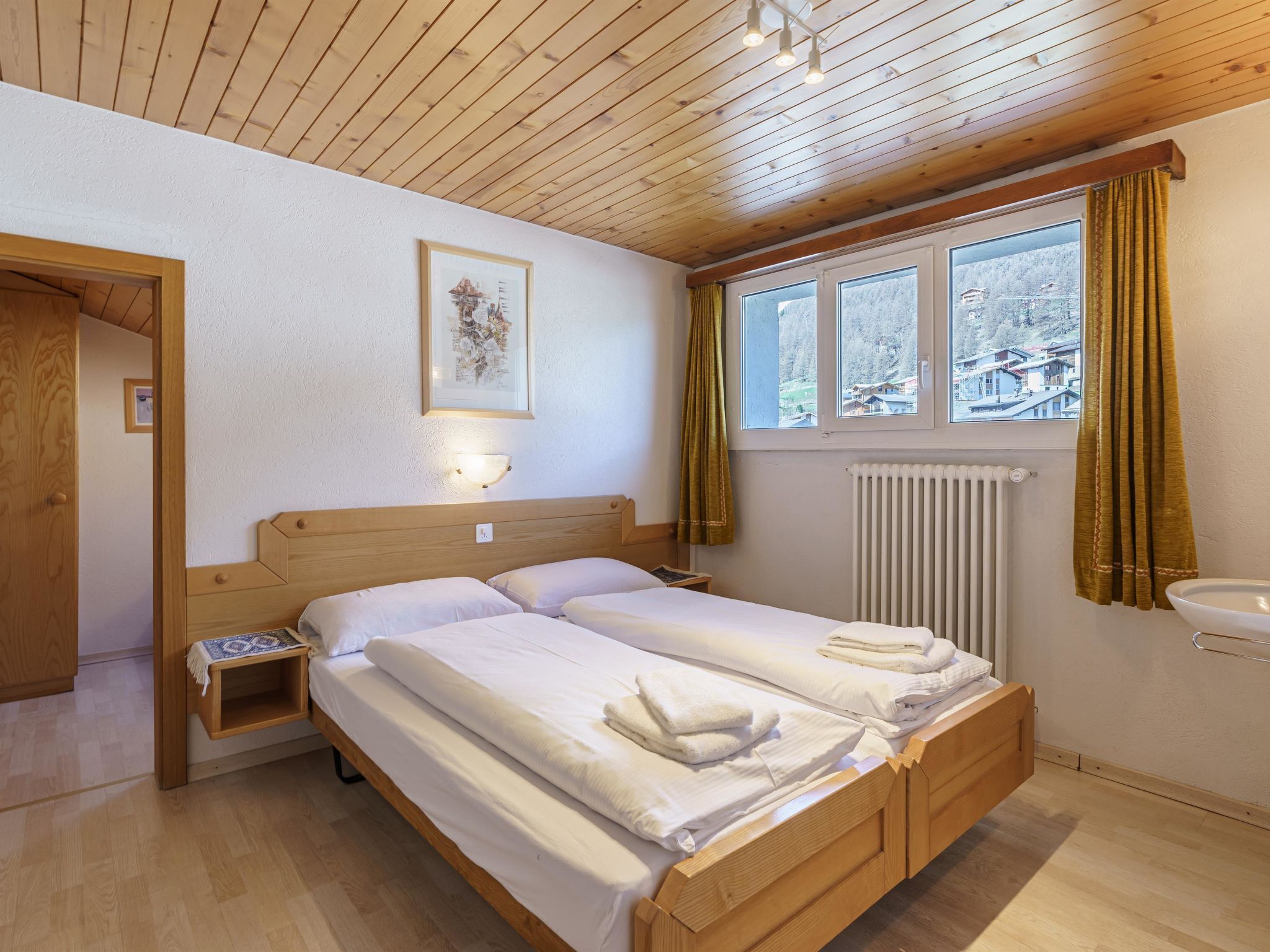 A hotel room with a wooden ceiling, a bed with white linens, a nightstand, a framed picture on the wall, and a window with curtains.
