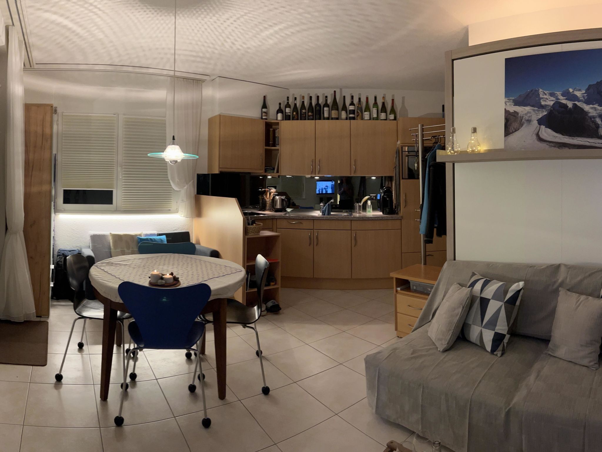 Een moderne woonkamer met een grijze bank, een eettafel met stoelen en een keuken met houten kasten en een televisie.