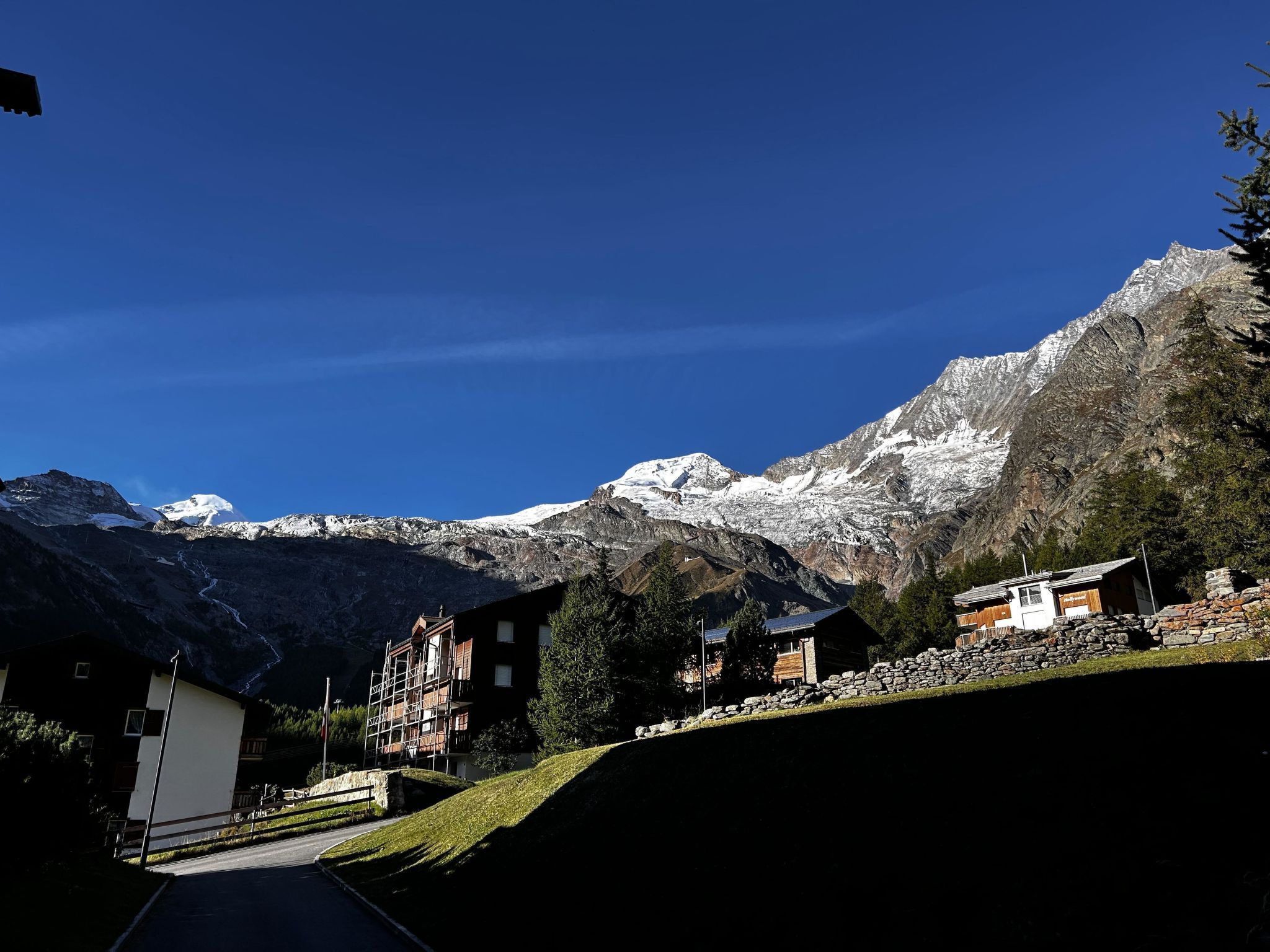 A mountain lodge with a view of snow-capped peaks, a paved road, and a stone wall.
