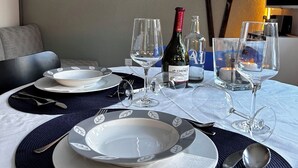 Een eettafel gedekt met borden, glazen, bestek, een fles wijn, en een schilderij van bergen aan de muur.