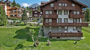 A multi-story wooden building with balconies, surrounded by greenery and mountains in the background. - Maria Appartement/Fewo 4-Bettwohnung Nr. 4 by Interhome (Saas-Fee)