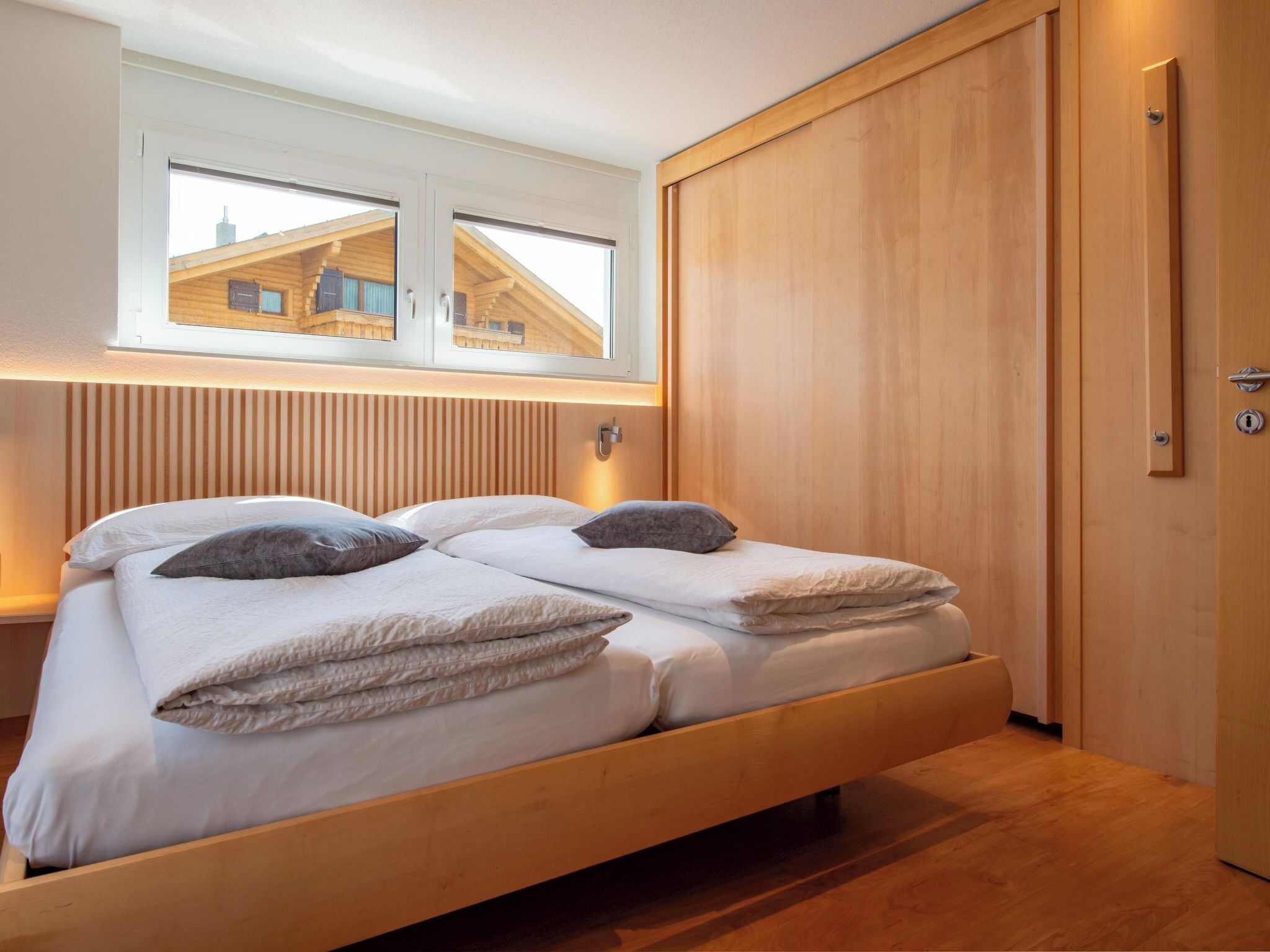 A modern bedroom with a wooden bed, a window with a view, and a wooden wardrobe.
