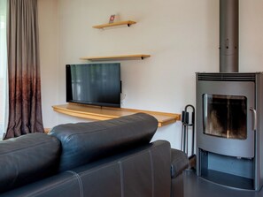 Un salon moderne avec un canapé en cuir noir, un téléviseur à écran plat posé sur une étagère en bois et un poêle à bois.