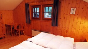 Et hyggeligt værelse i en træhytte med to senge, en stol, et bord og et vindue med gardiner.