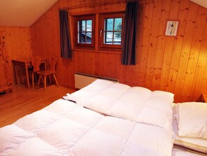 A wooden cabin room with two beds, a chair, a table, and a window with curtains. - Chalet Heimeli Appartement/Fewo 6-Bettwohnung by Interhome (Saas-Fee)