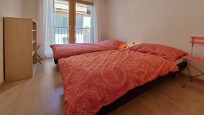Ein Zimmer mit zwei Betten, einem Schrank, einem Balkon und einer gelben Pendelleuchte.