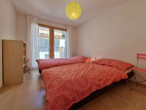 Ein Zimmer mit zwei Betten, einem Schrank, einem Balkon und einer gelben Pendelleuchte.