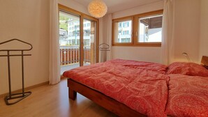 Ein Schlafzimmer mit einem Bett, einer Hängelampe, einem Fenster und Blick auf Gebäude.