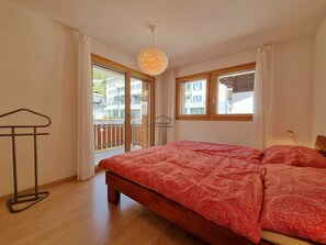 Ein Schlafzimmer mit einem Bett, einer Hängelampe, einem Fenster und Blick auf Gebäude.