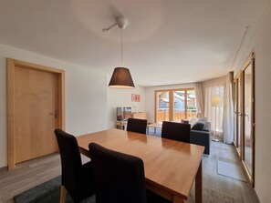 Un comedor moderno con una mesa y sillas de madera, una lámpara colgante y vistas a un balcón con sofá.