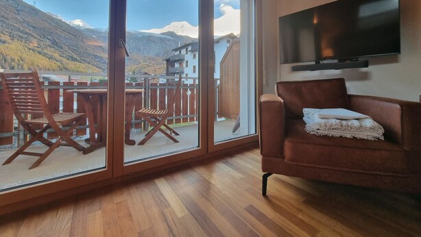 Una sala de estar con un sofá, un televisor y un balcón con vistas a montañas.