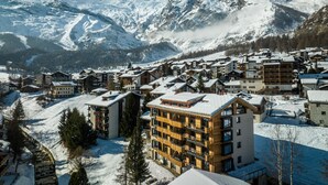 A snow-covered mountain town with modern buildings, including a prominent multi-story hotel with balconies. - Riverside 24 Appartement/Fewo Appartement/Fewo by Interhome (Saas-Fee)