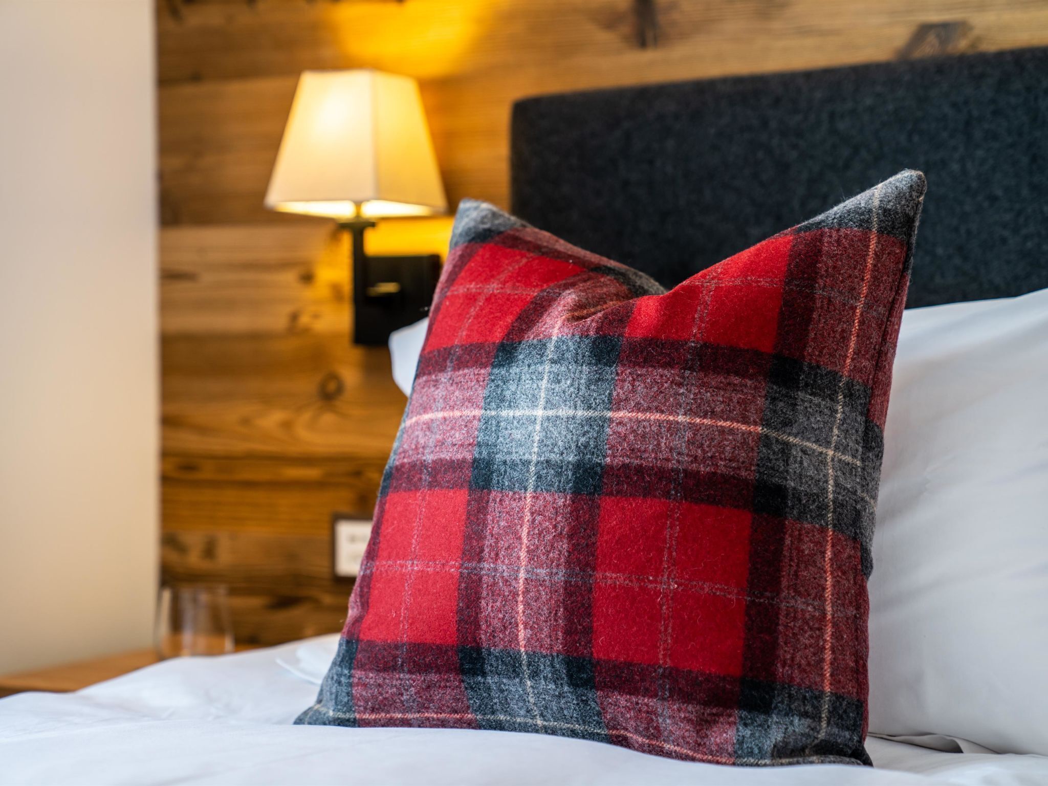 A bed with a red and black plaid pillow, a white pillow, and a wooden headboard.