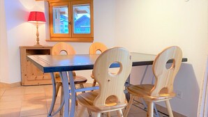 Un coin repas avec une table et des chaises en bois, une fenêtre avec des stores et une lampe.