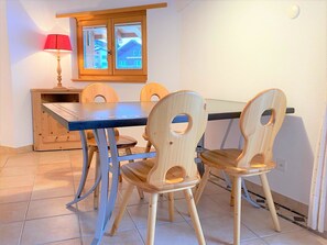 A dining area with a wooden table and chairs, a window with blinds, and a lamp. - Dominic B Appartement/Fewo 4-Bettwohnung by Interhome (Saas-Fee)