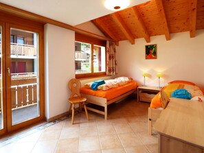 A bedroom with a bed, a chair, a nightstand, and a window with curtains. - Dominic B Appartement/Fewo 4-Bettwohnung by Interhome (Saas-Fee)