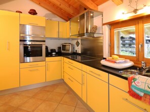 A kitchen with yellow cabinets, stainless steel appliances, a black countertop, and a window with a view. - Dominic B Appartement/Fewo 4-Bettwohnung by Interhome (Saas-Fee)