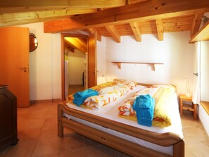 A bedroom with a wooden bed, a bedside table, a lamp, and a door leading to another room. - Dominic B Appartement/Fewo 4-Bettwohnung by Interhome (Saas-Fee)