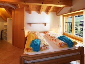 A bedroom with two beds, a wooden ceiling, a window with a view, and a door leading to a bathroom. - Dominic B Appartement/Fewo 4-Bettwohnung by Interhome (Saas-Fee)