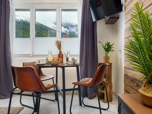 Een eetgedeelte met een tafel gedekt voor twee personen, twee leren stoelen, een schaal fruit, een glas water en een vaas met gedroogde planten.