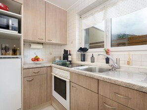 A compact kitchen with wooden cabinets, a built-in oven, a sink, and a window with a view. - Falke EG Appartement/Fewo Greenspot Apartment by Interhome (Saas-Fee)