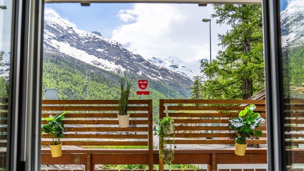 A window view of a mountain landscape with a wooden fence and potted plants. - Falke EG Appartement/Fewo Greenspot Apartment by Interhome (Saas-Fee)