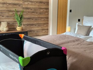 A room with a bed, a nightstand, a potted plant, and a baby playpen. - Falke EG Appartement/Fewo Greenspot Apartment by Interhome (Saas-Fee)