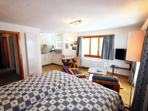 A room with a bed, a small table, a chair, a sofa, a window with curtains, and a kitchenette in the background. - La Sapinière Appartement/Fewo 2-Bettwohnung by Interhome (Saas-Fee)