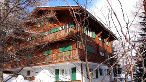 Un edificio de madera de varios pisos con balcones, contraventanas verdes y un basamento de piedra.