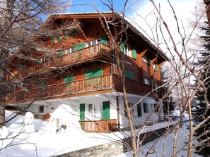 A multi-story wooden building with balconies, green shutters, and a stone foundation. - La Sapinière Appartement/Fewo 2-Bettwohnung by Interhome (Saas-Fee)