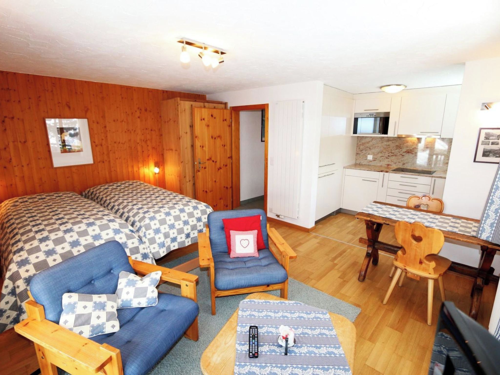 A room with two beds, a chair, a table, a microwave, and a kitchenette.