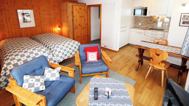 Una habitación con dos camas, una silla, una mesa, microondas y un rincón americano.
