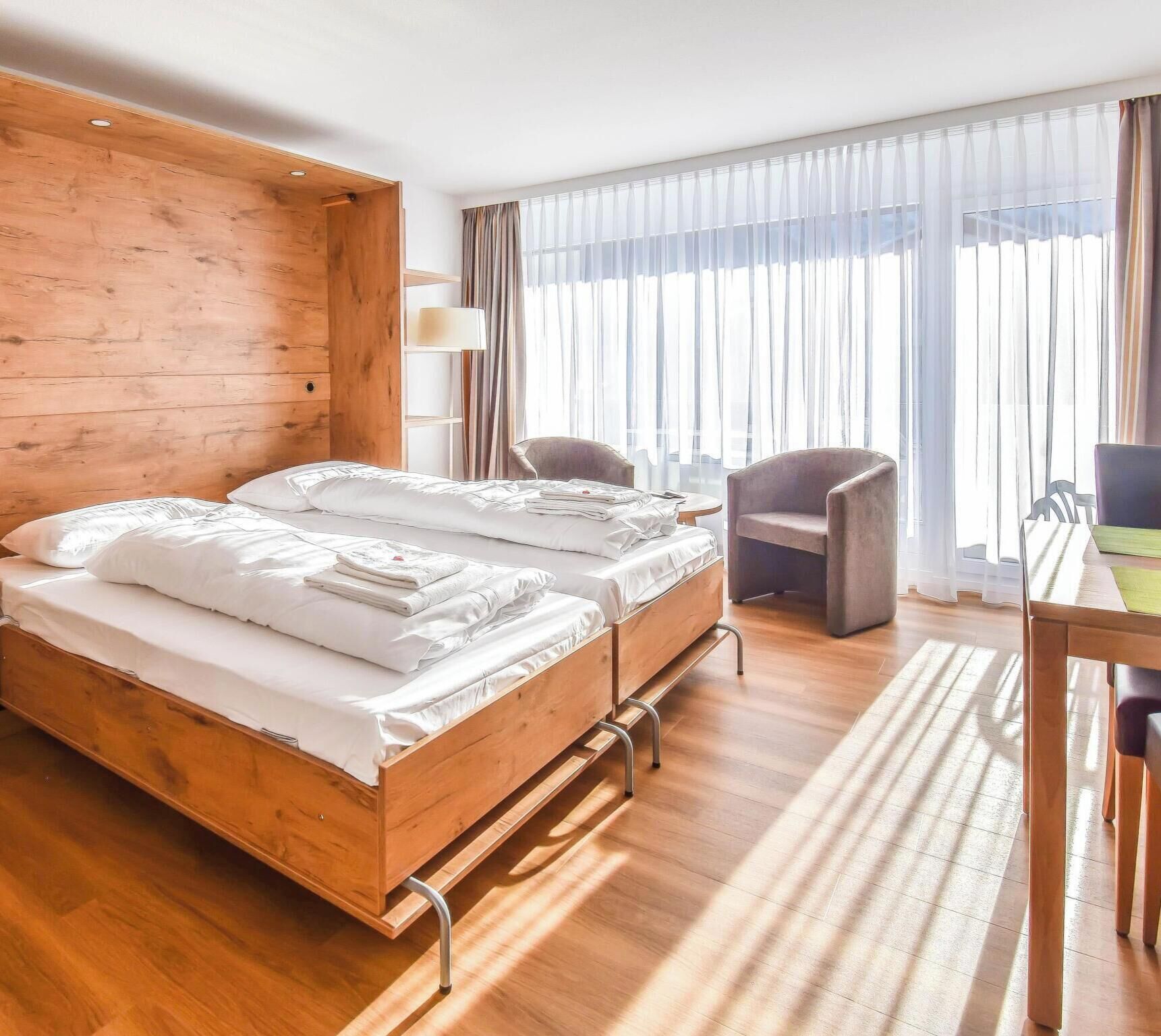 Un lit double avec une tête de lit en bois, un bureau avec une chaise et une fenêtre avec des rideaux.