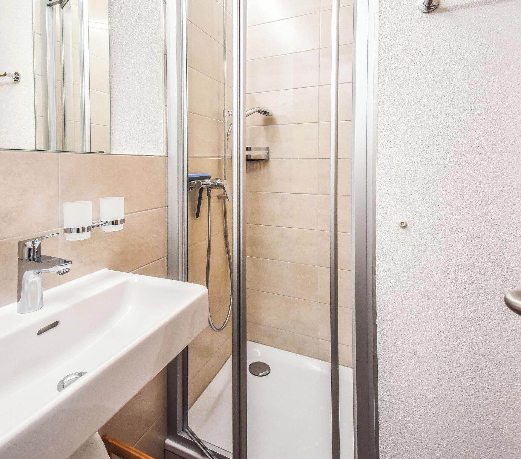 Um banheiro moderno com box de vidro, pia branca e azulejos bege.