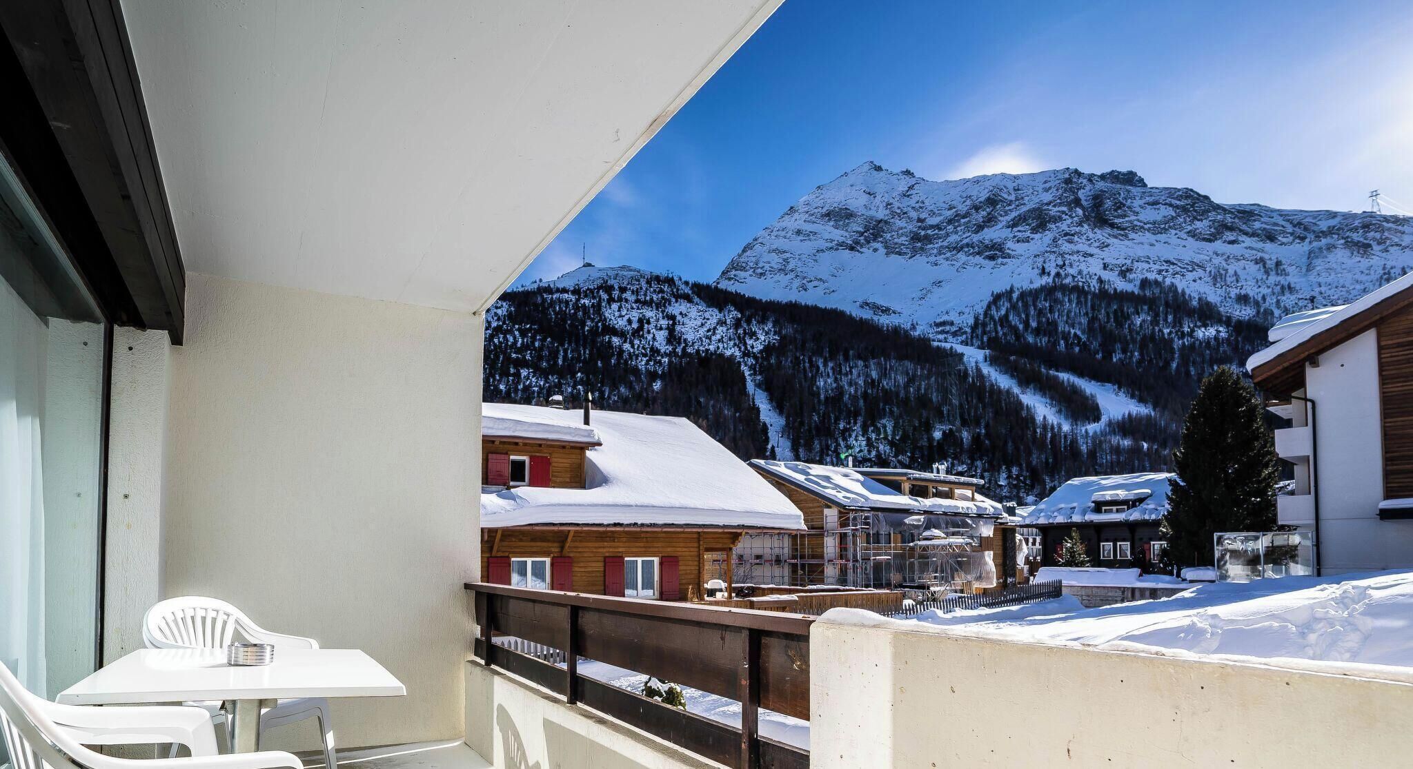 A balcony with a view of snow-covered mountains and buildings.