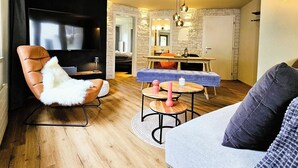 A modern living room with a flat-screen TV, a leather armchair, a sofa, a dining area with a table and chairs, and a stone accent wall. - Achat 4 Appartement/Fewo 4-Bettwohnung by Interhome (Saas-Fee)