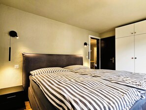 A bedroom with a bed, a nightstand, a wardrobe, and a door leading to another room. - Achat 4 Appartement/Fewo 4-Bettwohnung by Interhome (Saas-Fee)