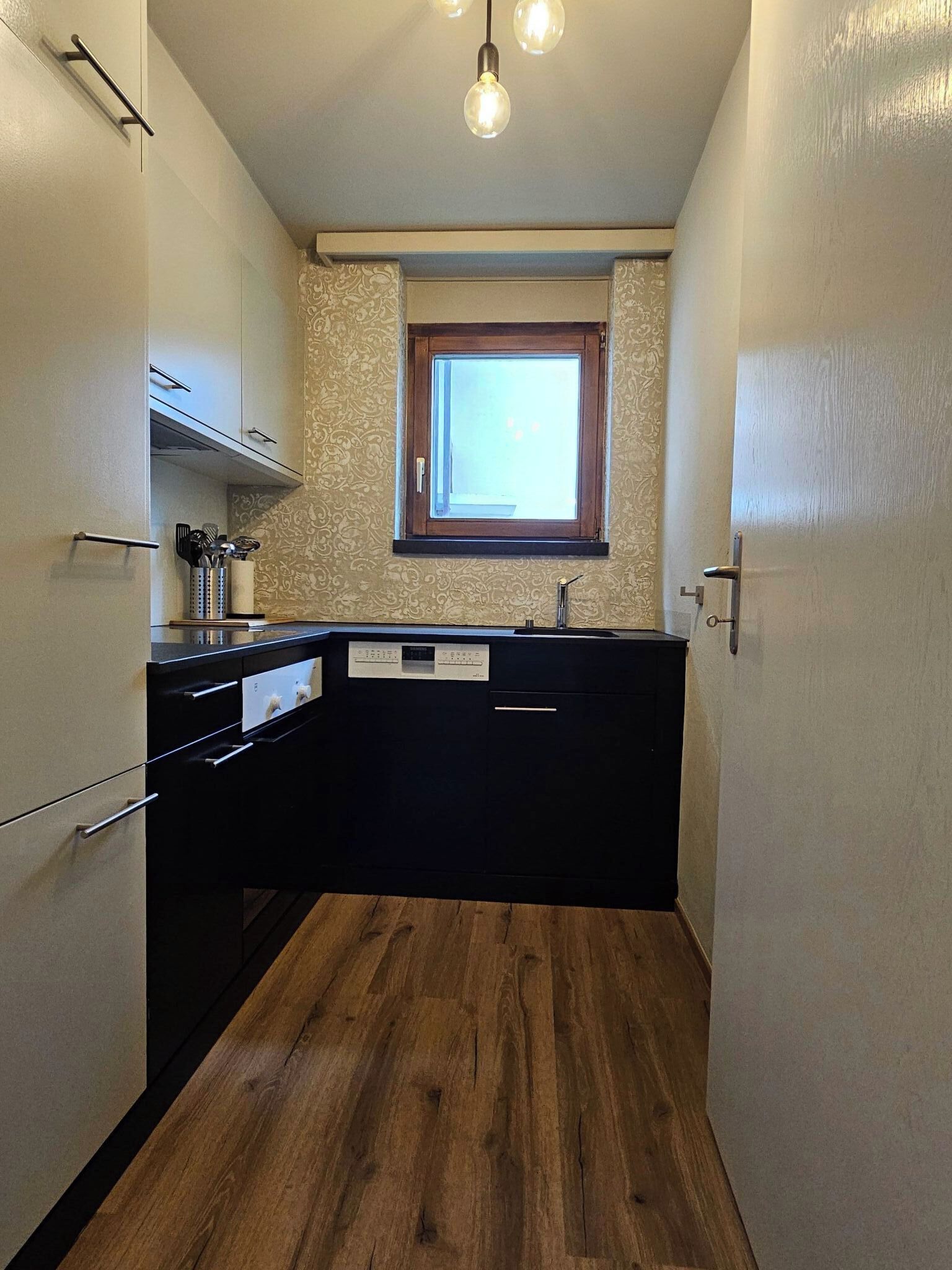 A compact kitchen with a window, wooden flooring, and a built-in oven.