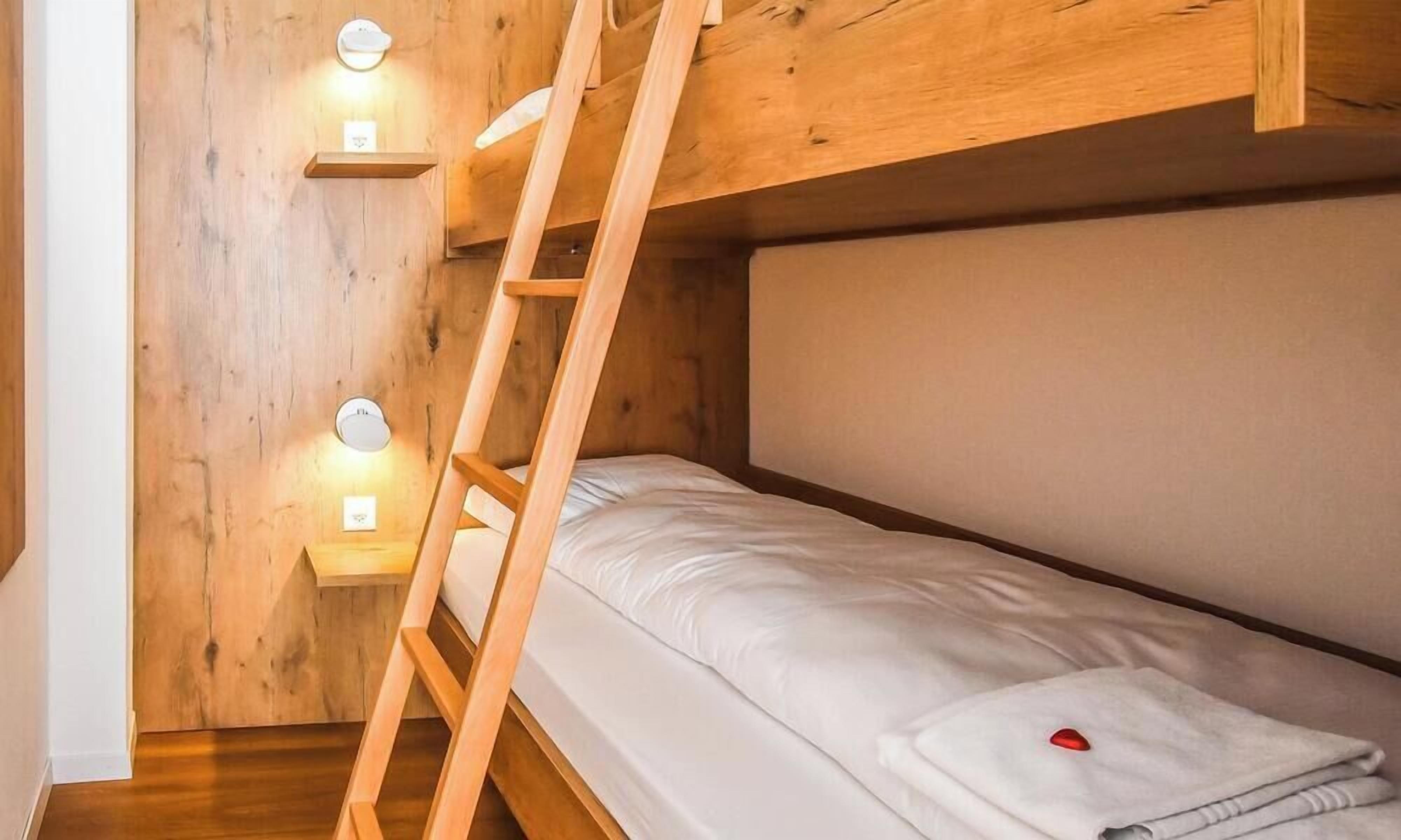 Ein Etagenbett mit Holzleiter, einem kleinen Regal und zwei Wandleuchten.