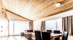 A modern interior with a wooden ceiling, a sofa, a dining table with chairs, and large windows with curtains. - Haus Camillo Appartement/Fewo 6-Bettwohnung Nr. 24 by Interhome (Saas-Fee)