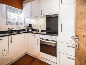 A modern kitchen with white cabinets, a black countertop, a coffee maker, and an oven. - Haus Camillo Appartement/Fewo 6-Bettwohnung Nr. 24 by Interhome (Saas-Fee)