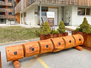 Ein Hotelzugang mit einer Rezeption, einer Lounge und einem Geschäft. Holzpflanzgefäße mit Grünpflanzen sowie eine markante Holzskulptur sind zu sehen.
