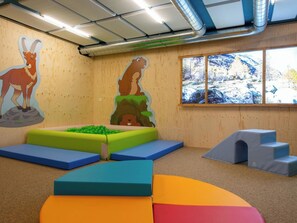 A playroom with a wooden wall, a window with a view of a rocky landscape, and colorful play mats. - Casa Antares – Montela Holiday Stay Appartement/Fewo by Interhome (Saas-Grund)