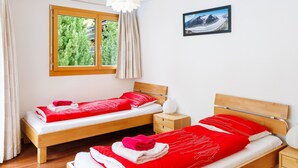 Hotelkamer met twee bedden, een raam met uitzicht op groen, een foto aan de muur en een witte plafondlamp.