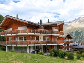Eine zweistöckige Holzhütte mit Balkonen vor einer Bergkulisse.