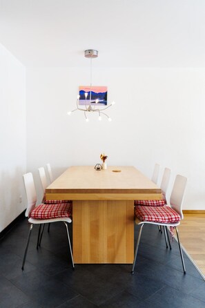 Ein Essbereich mit einem Holztisch, weißen Stühlen, einer Pendelleuchte und einem gerahmten Bild an der Wand.