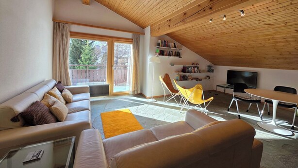 Un salon confortable avec un canapé, une table basse, un fauteuil jaune, une bibliothèque et un téléviseur.